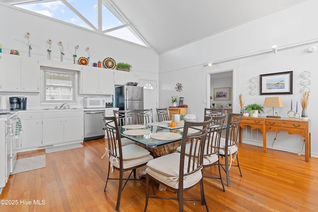 dining space with light wood-type flooring, sink, and high vaulted ceiling