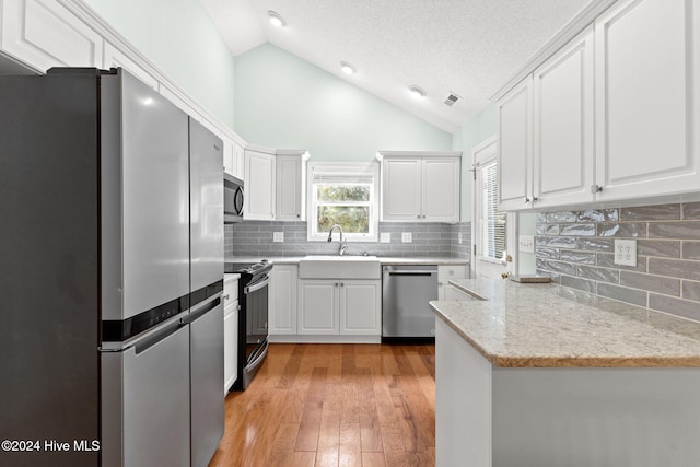 kitchen with lofted ceiling, light wood-style flooring, a sink, white cabinets, and appliances with stainless steel finishes