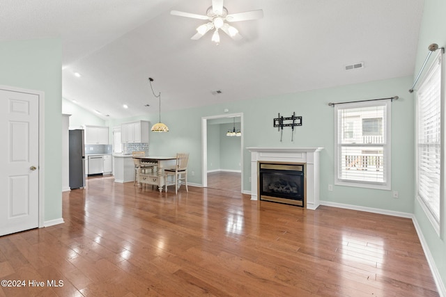 unfurnished living room with lofted ceiling, light wood finished floors, a glass covered fireplace, and visible vents