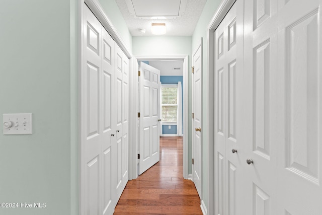 hallway with a textured ceiling, baseboards, and wood finished floors