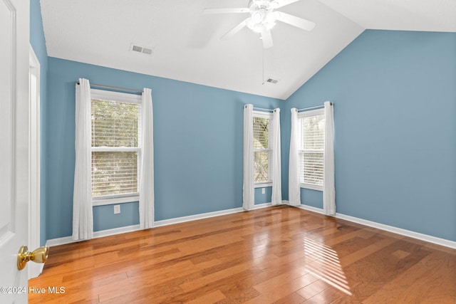 empty room featuring lofted ceiling, plenty of natural light, visible vents, and hardwood / wood-style floors