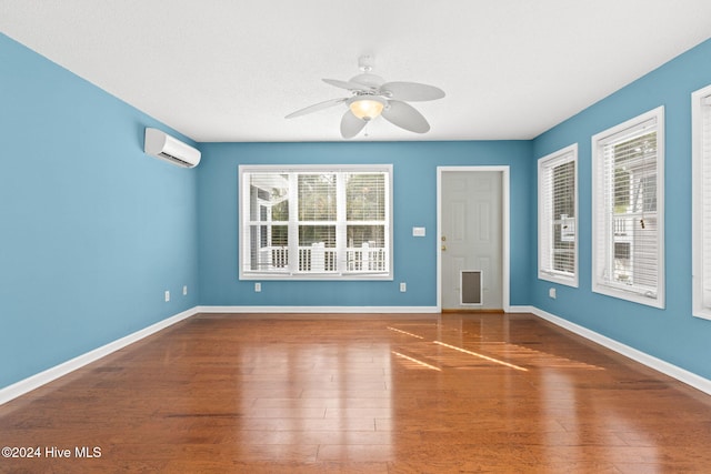 empty room with wood finished floors, ceiling fan, baseboards, and a wall mounted AC