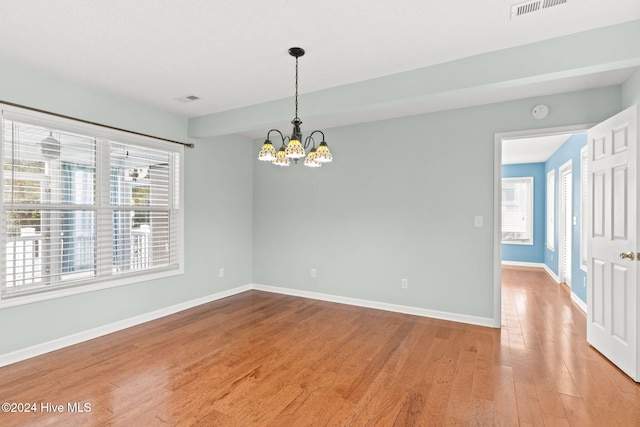 empty room featuring an inviting chandelier, visible vents, baseboards, and wood finished floors