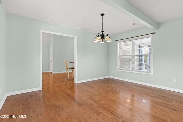 spare room featuring a chandelier, beam ceiling, baseboards, and wood finished floors