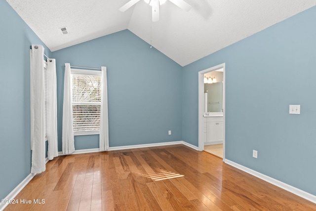 unfurnished bedroom with lofted ceiling, a textured ceiling, visible vents, baseboards, and hardwood / wood-style floors