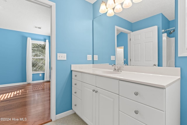 bathroom featuring a notable chandelier, visible vents, vanity, a textured ceiling, and baseboards