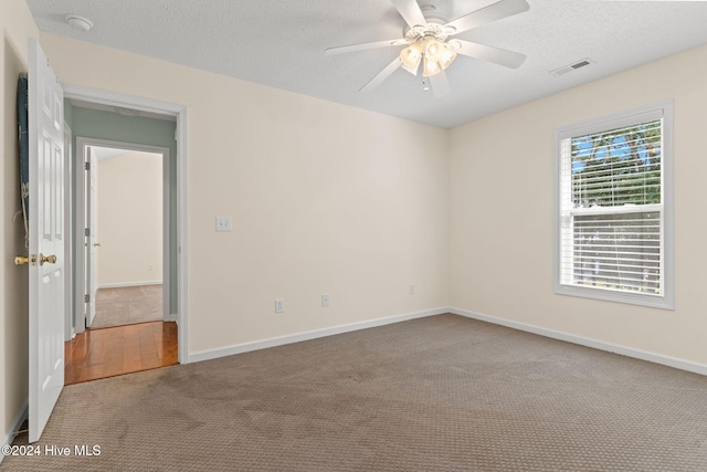 carpeted empty room featuring a textured ceiling, a ceiling fan, visible vents, and baseboards