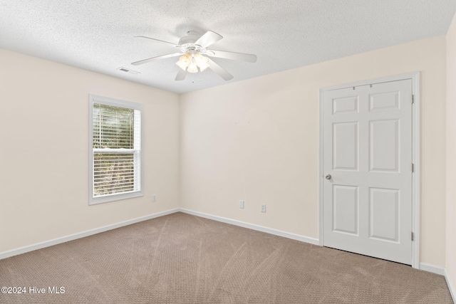 spare room featuring a textured ceiling, baseboards, visible vents, and light colored carpet