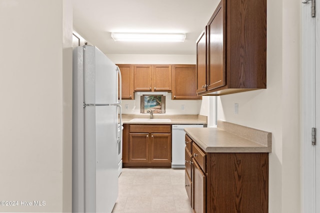 kitchen with white appliances, light countertops, a sink, and brown cabinetry