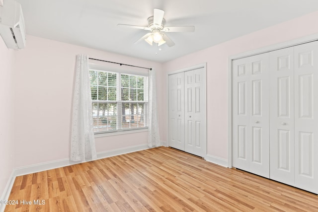 unfurnished bedroom featuring light wood finished floors, two closets, a wall mounted AC, a ceiling fan, and baseboards