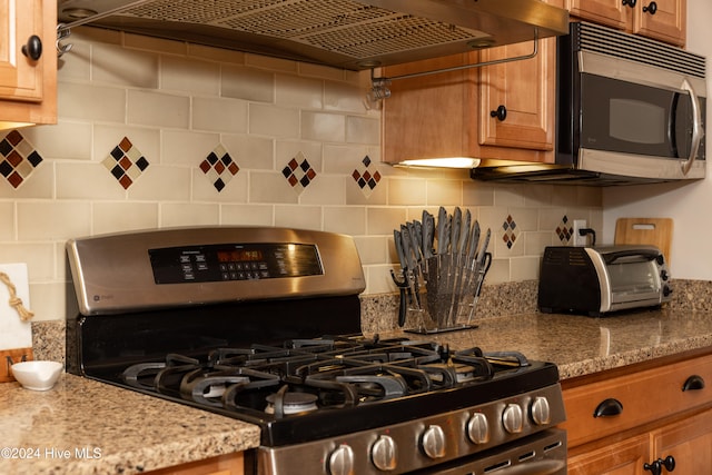 kitchen with light stone counters, tasteful backsplash, appliances with stainless steel finishes, and exhaust hood