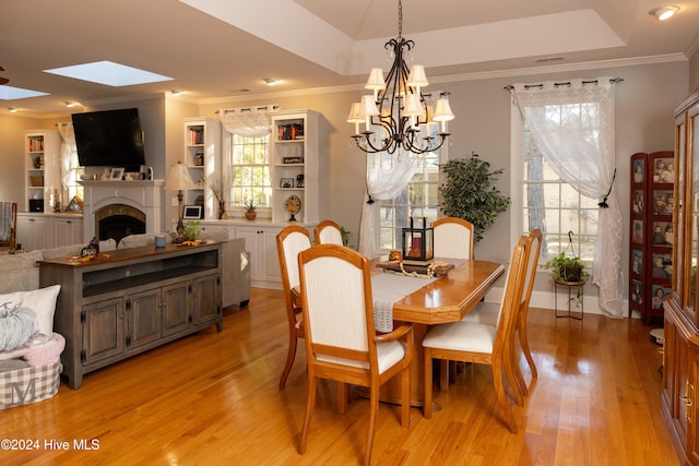 dining area featuring light hardwood / wood-style floors, a skylight, a raised ceiling, and a wealth of natural light