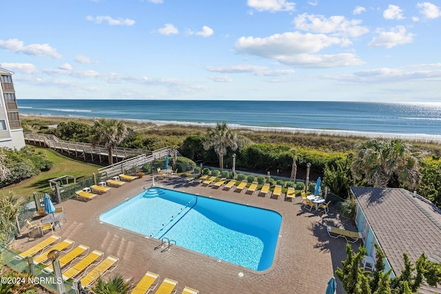 view of swimming pool with a water view, a patio area, and a beach view