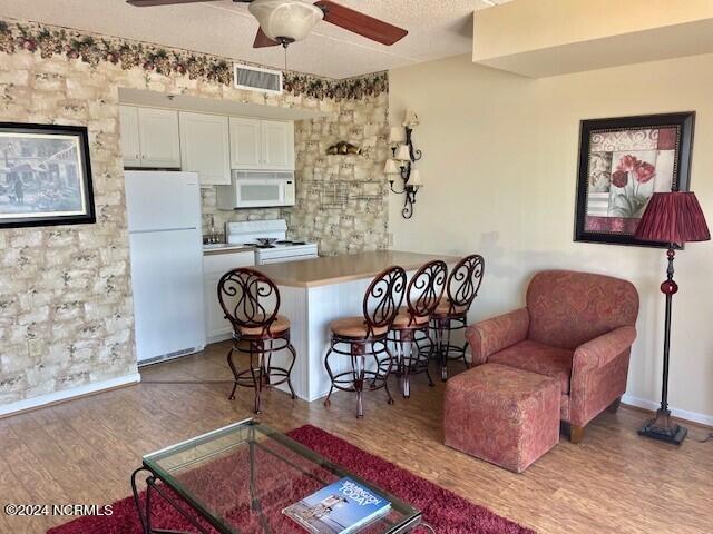 kitchen featuring white cabinets, ceiling fan, a breakfast bar, light hardwood / wood-style floors, and white appliances