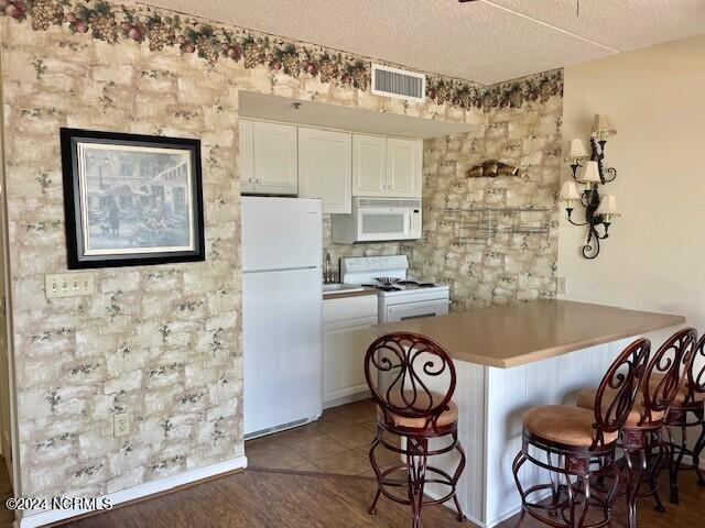 kitchen with a breakfast bar area, white cabinets, dark hardwood / wood-style floors, and white appliances