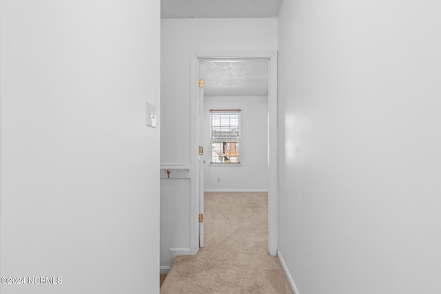 corridor with a textured ceiling and light colored carpet