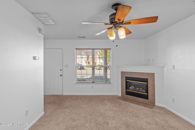 unfurnished living room with a tiled fireplace, ceiling fan, and light carpet