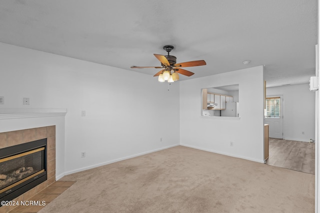 unfurnished living room featuring a tiled fireplace, light colored carpet, and ceiling fan