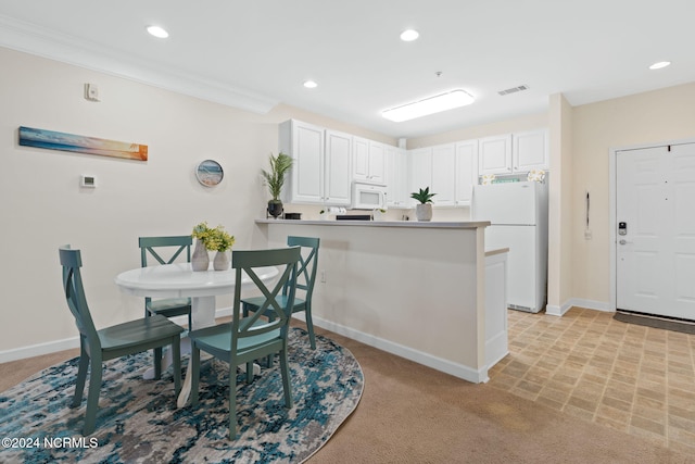 kitchen with kitchen peninsula, ornamental molding, light colored carpet, white cabinetry, and white appliances