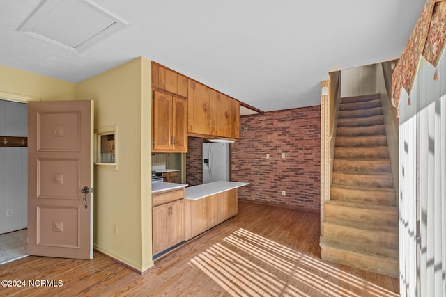 kitchen featuring light hardwood / wood-style flooring, brick wall, and white refrigerator with ice dispenser