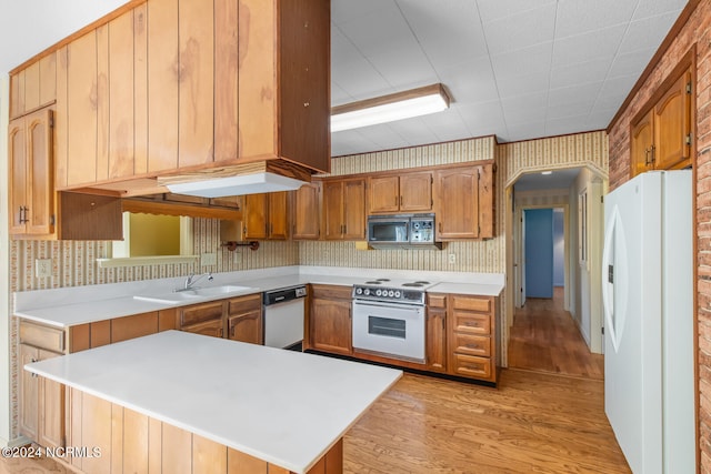 kitchen featuring kitchen peninsula, white appliances, brick wall, sink, and light hardwood / wood-style floors