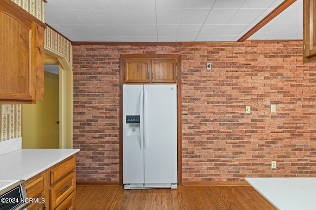 kitchen with light hardwood / wood-style flooring, brick wall, and white refrigerator with ice dispenser