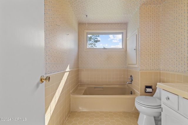 bathroom with tile walls, toilet, a washtub, vanity, and tile patterned floors