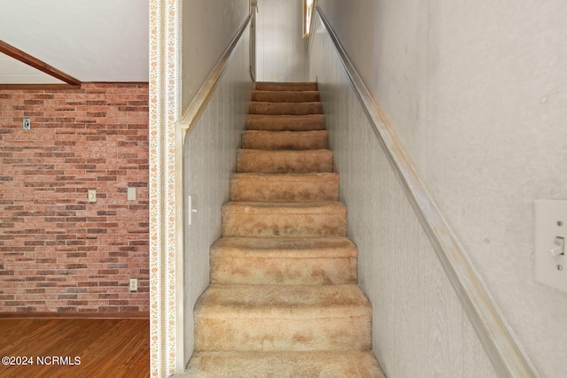 stairs featuring brick wall and wood-type flooring