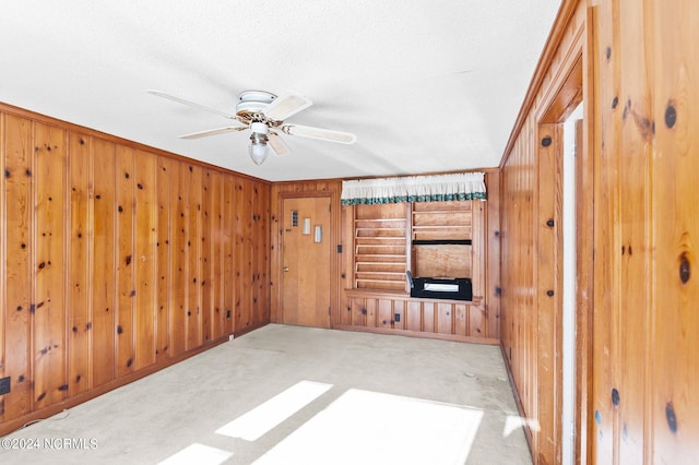 carpeted living room featuring ceiling fan, crown molding, a textured ceiling, and wooden walls