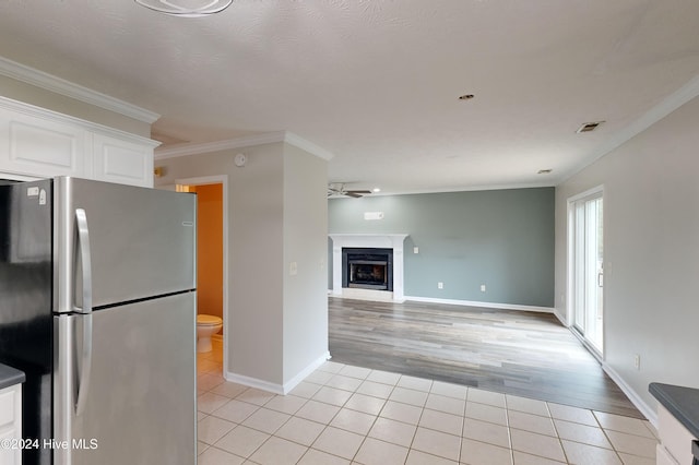 kitchen featuring light hardwood / wood-style floors, a textured ceiling, ornamental molding, white cabinetry, and stainless steel fridge