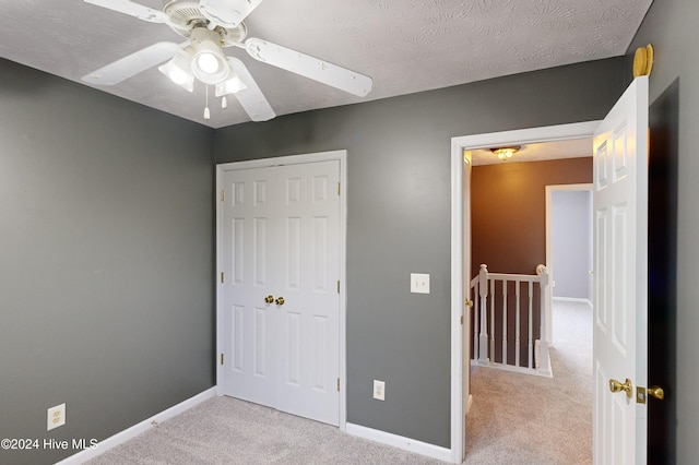 unfurnished bedroom featuring ceiling fan, a textured ceiling, light carpet, and a closet