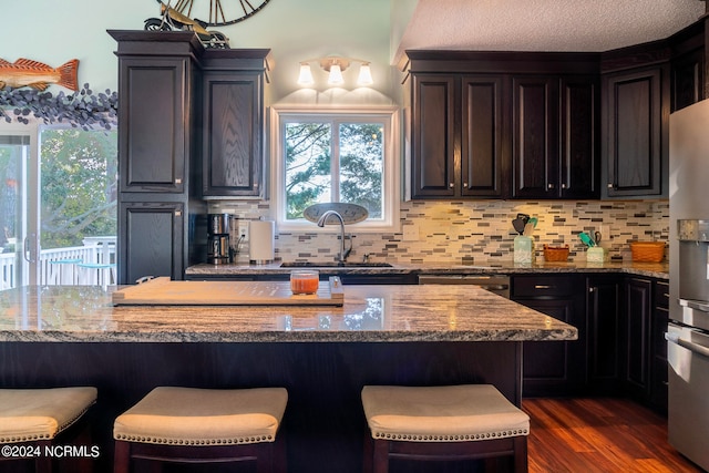 kitchen featuring light stone countertops, dark wood-type flooring, a kitchen bar, and stainless steel fridge with ice dispenser