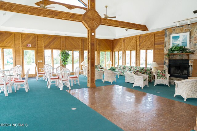 unfurnished dining area featuring a stone fireplace, wood walls, ceiling fan, and a wealth of natural light