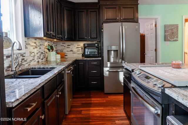 kitchen with dark brown cabinetry, dark wood-type flooring, appliances with stainless steel finishes, and light stone counters