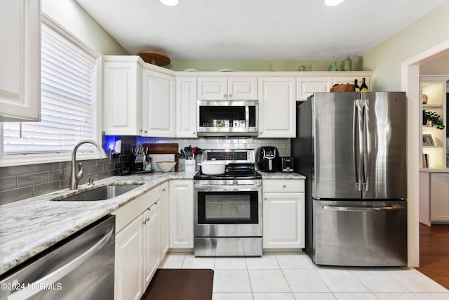 kitchen with white cabinetry, light stone countertops, stainless steel appliances, and sink