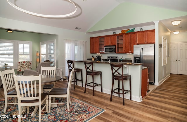 kitchen featuring a kitchen breakfast bar, vaulted ceiling, stainless steel appliances, and light hardwood / wood-style floors