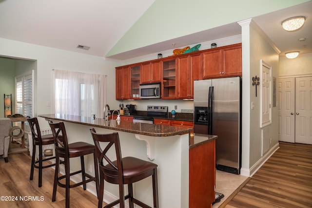 kitchen featuring light wood-type flooring, an island with sink, stainless steel appliances, vaulted ceiling, and a breakfast bar