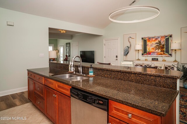 kitchen with dark stone countertops, a center island with sink, sink, stainless steel dishwasher, and light hardwood / wood-style floors