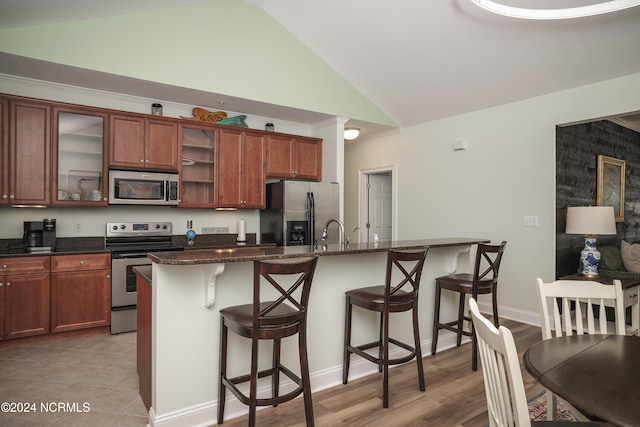kitchen with stainless steel appliances, lofted ceiling, a kitchen bar, a kitchen island with sink, and glass insert cabinets