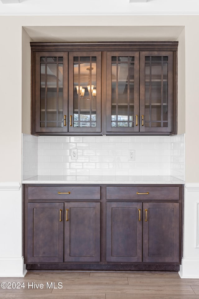 bar with decorative backsplash, hardwood / wood-style floors, and dark brown cabinetry