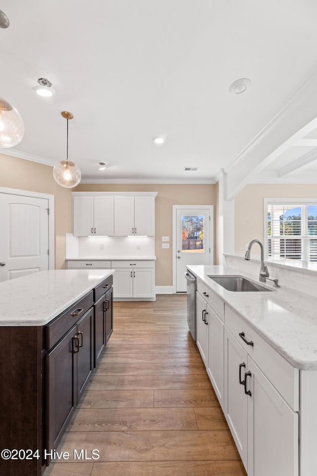 kitchen with light hardwood / wood-style flooring, hanging light fixtures, ornamental molding, sink, and white cabinetry