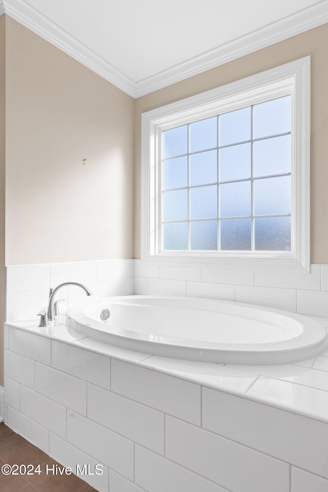 bathroom featuring a wealth of natural light, ornamental molding, and tiled bath