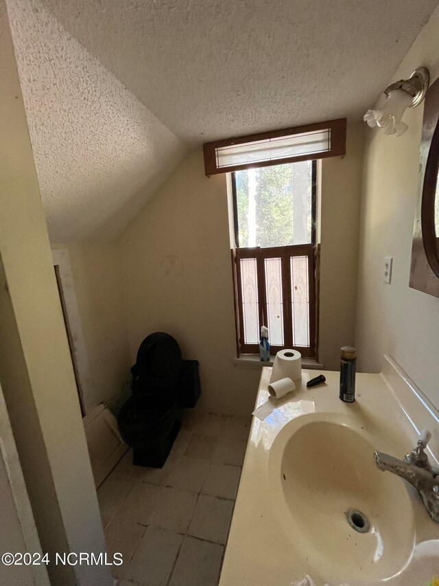 bathroom with vanity, lofted ceiling, a textured ceiling, and tile patterned floors