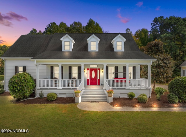 cape cod home with covered porch and a yard