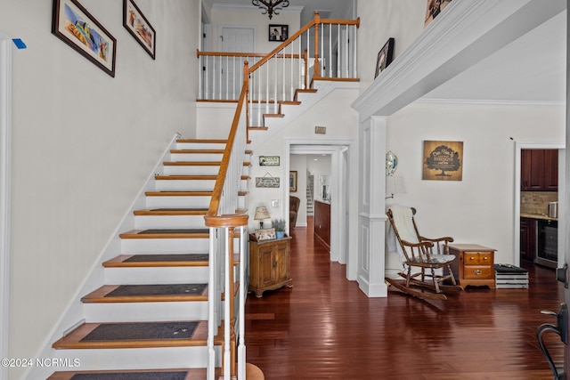 stairway featuring ornamental molding, a high ceiling, wood-type flooring, and beverage cooler