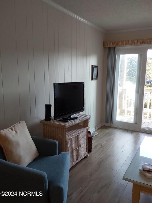 living room with wood walls, wood-type flooring, and ornamental molding