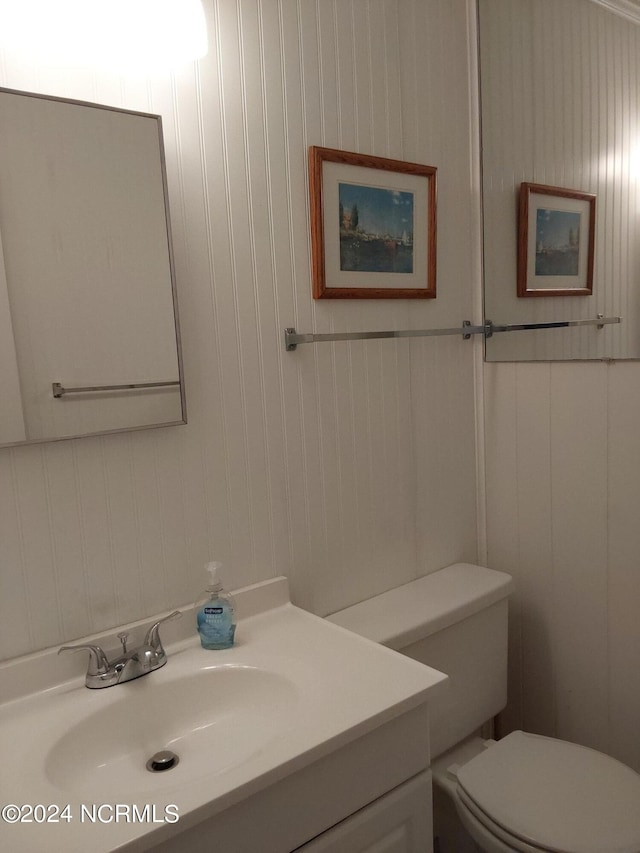 bathroom featuring toilet, wood walls, and vanity