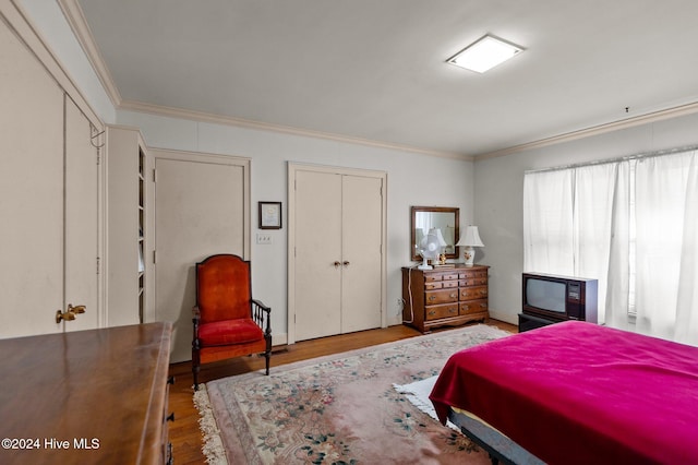 bedroom with crown molding, multiple closets, and light wood-type flooring