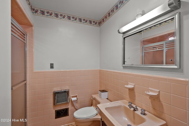 bathroom featuring toilet, a shower with shower door, sink, and tile walls