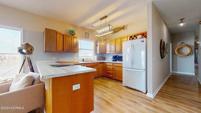 kitchen featuring kitchen peninsula, light wood-type flooring, pendant lighting, white fridge, and sink